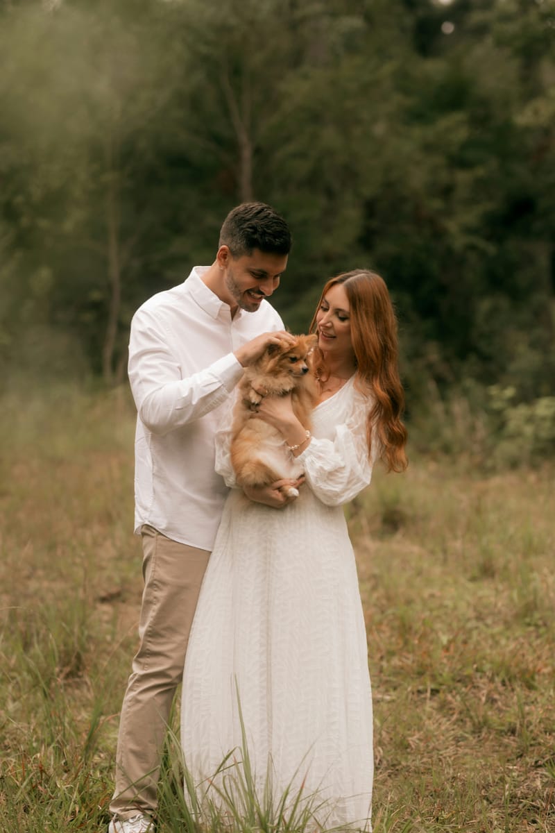 A couple cuddling their Pomeranian in a meadow