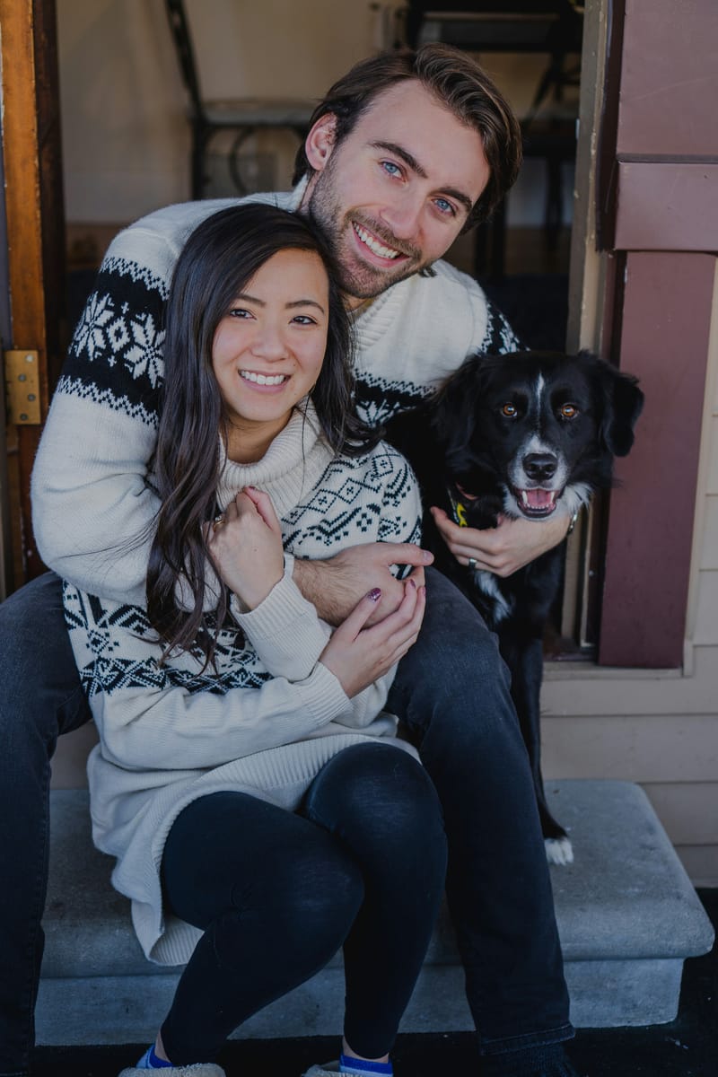 A smiling couple hugging their black and white dog on the porch