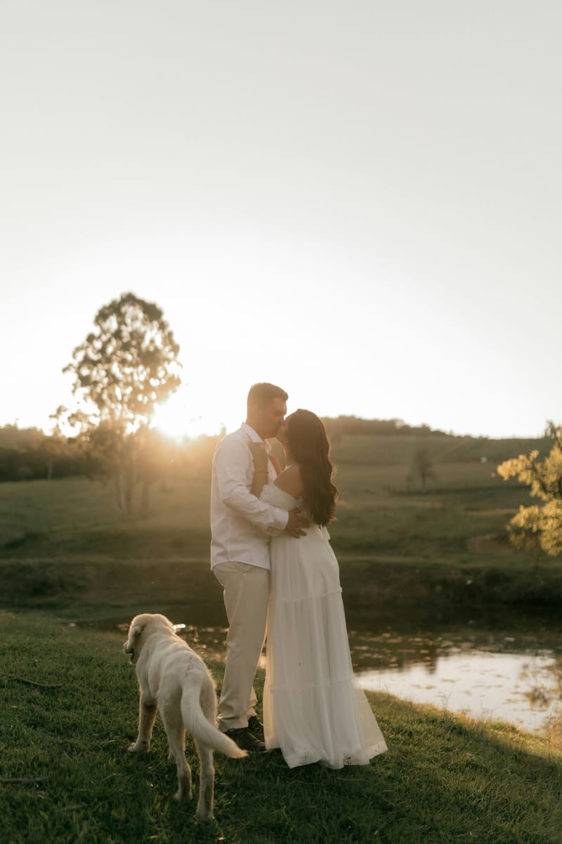 A couple sharing a kiss at sunset while their dog explores